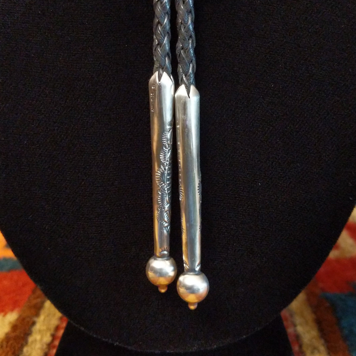 A close-up of a silver engraved details and spherical bead ends, hanging against a black display bust.