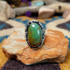 Handcrafted sterling silver ring featuring an elongated oval Royston turquoise cabochon with vivid green tones and golden-brown matrix, set in an ornate oxidized silver bezel with decorative bead accents.