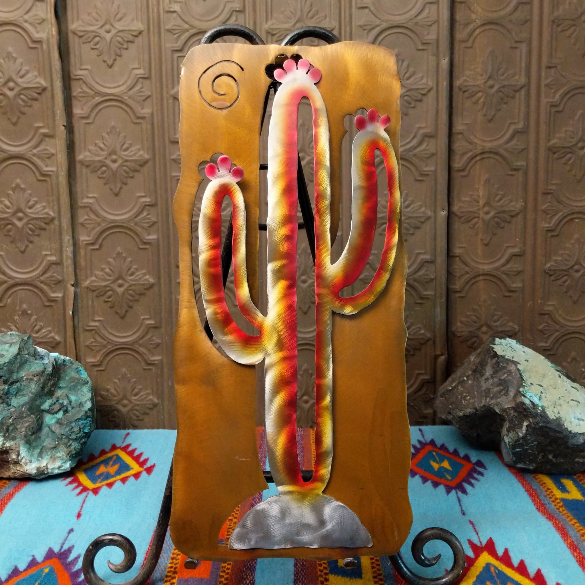 This 20-inch Crooks Design metal saguaro cactus features a red, yellow, and cream Sunset Swirl finish, silver-toned base, and warm golden-brown metal background.
