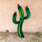 A large saguaro metal art piece featuring a vibrant green cactus with yellow streaks and red flowers.