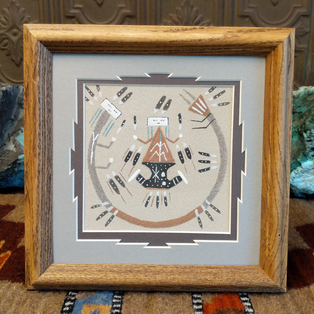 Different colored sand painting a picture of Father Sky and Mother Earth with protector set within a wooden frame.