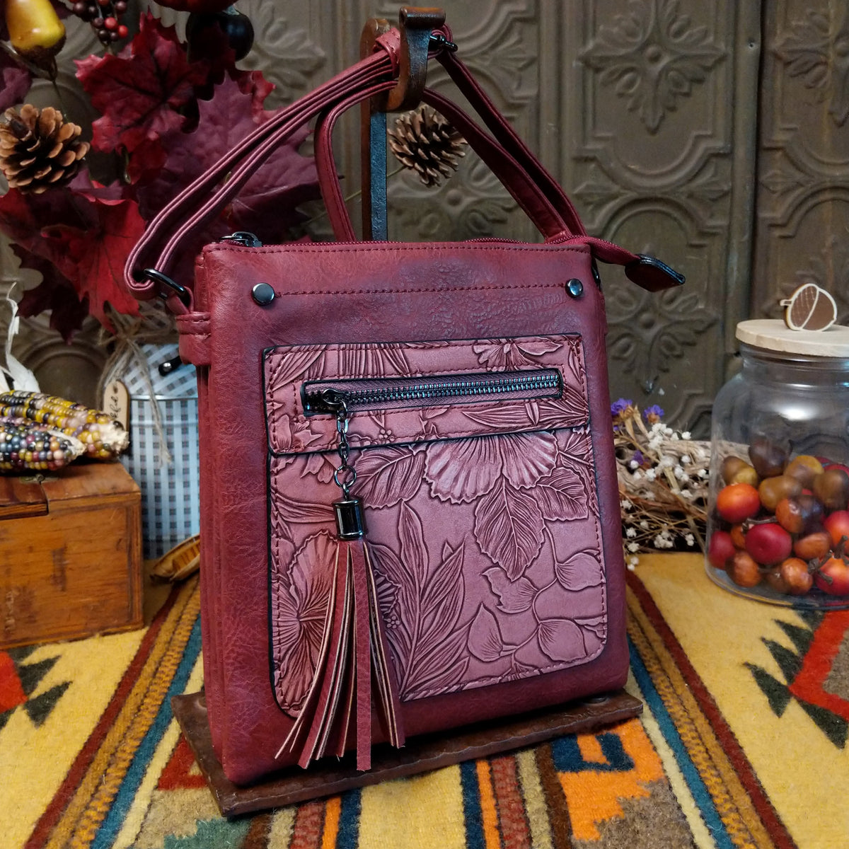 Sara Crossbody Bag by Liz Soto featuring a structured silhouette, embossed botanical front panel, zippered pocket, tassel zipper pull, top zip closure, and adjustable shoulder strap.