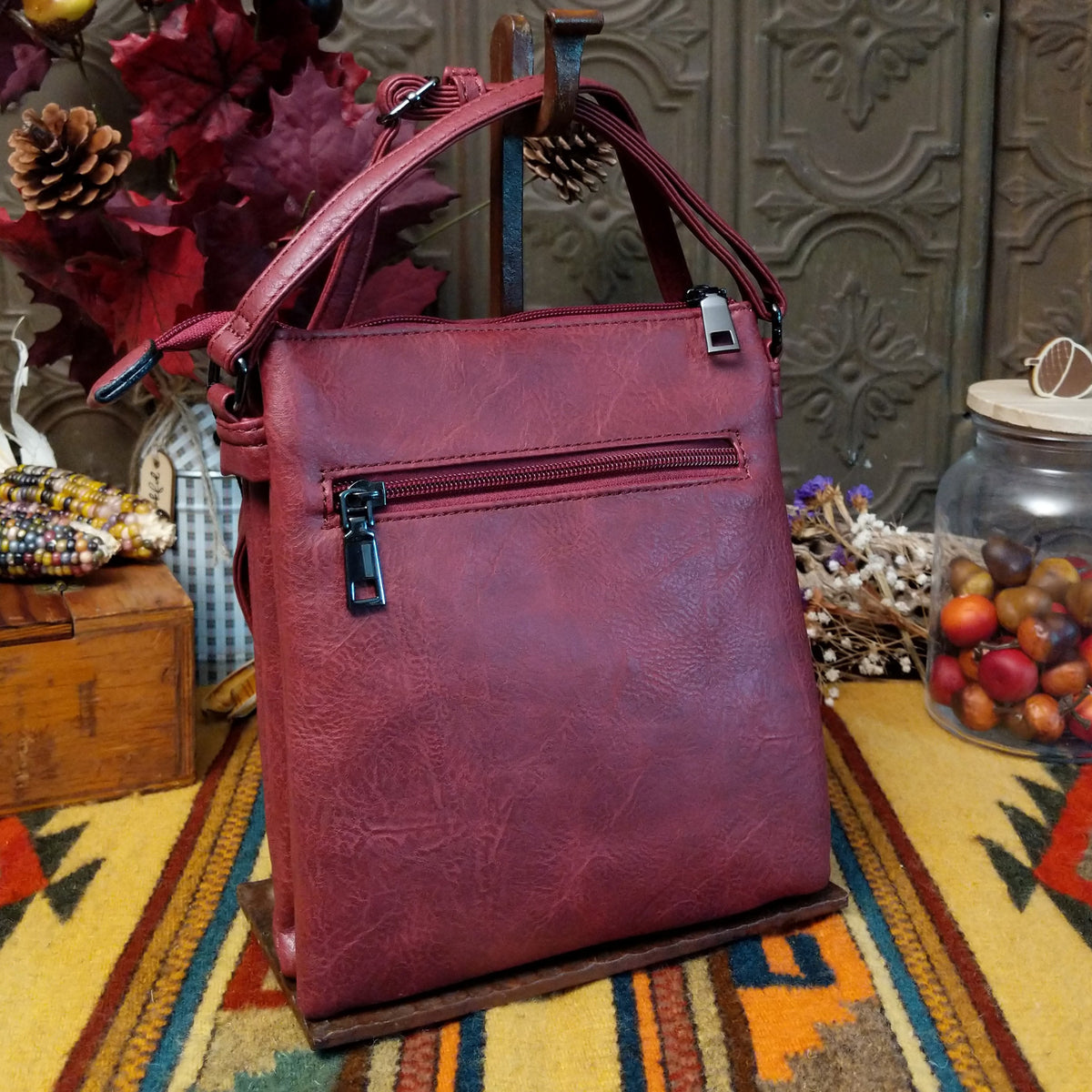 Sara Crossbody Bag by Liz Soto featuring a structured silhouette, embossed botanical front panel, zippered pocket, tassel zipper pull, top zip closure, and adjustable shoulder strap; back side.