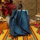 Selena Crossbody Bag by Liz Soto featuring embossed floral detailing, vintage-style kiss-lock frame closure, front zippered pocket, decorative tassel, and adjustable shoulder strap; back view.