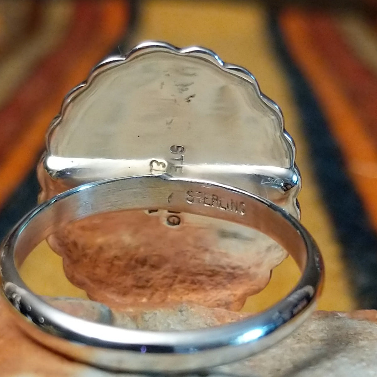 Silver Concho Ring by Elgin Tom featuring an oval silver concho with radiating stamped patterns, a raised diamond-shaped center, scalloped edges, and contrasting oxidized detailing; artisan and Sterling Silver stamp.