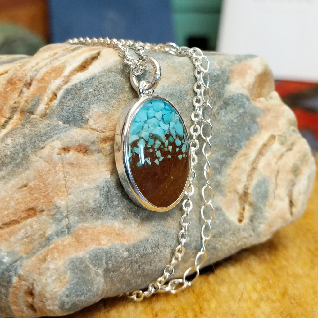 Oval necklace pendant with a silver-plated brass frame, showcasing turquoise and brown sand.
