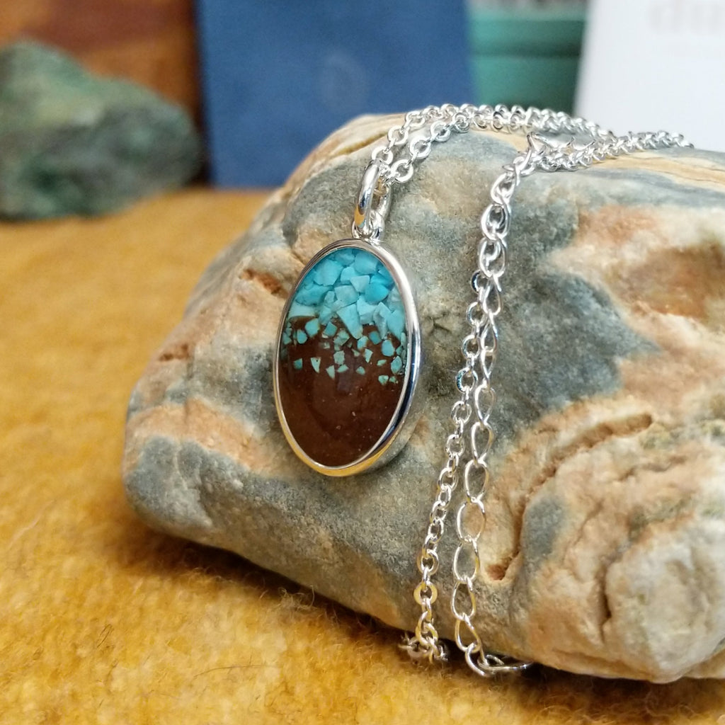 Oval necklace pendant with a silver-plated brass frame, showcasing turquoise and brown sand.