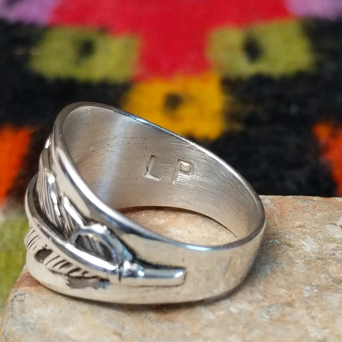 Wide silver feather ring by L.P. with detailed stamped lines and a raised center spine. Close up of the artist's stamped signature.
