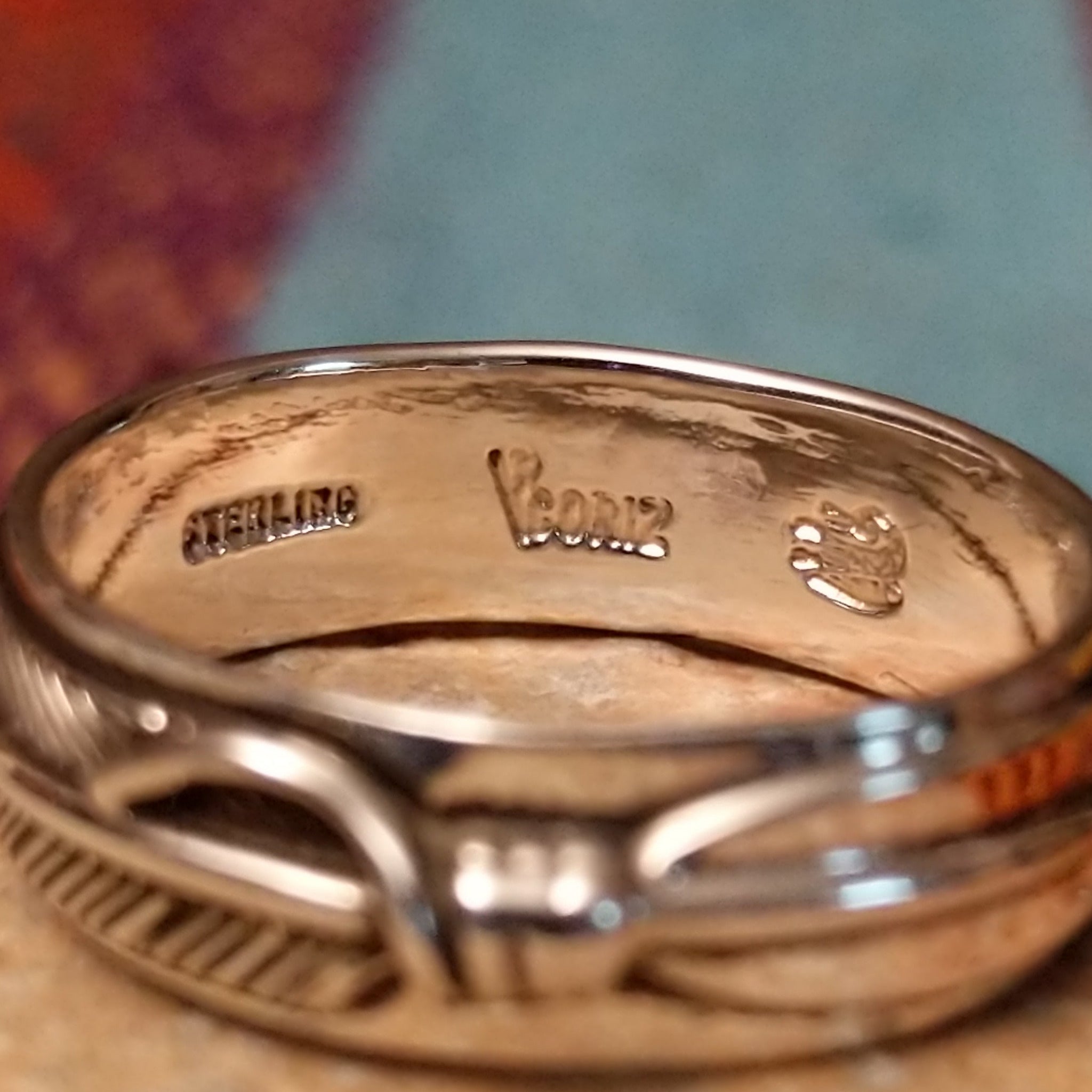 Silver Feather Ring by Raymond Coriz featuring a continuous detailed feather pattern with textured lines, darkened accents, and polished Sterling Silver borders; artisan and Sterling Silver stamp.