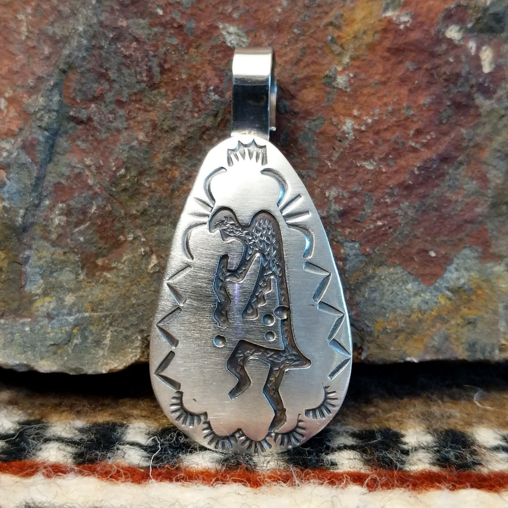 Triangular sterling silver pendant with kokopelli figure and geometric designs on the surface.