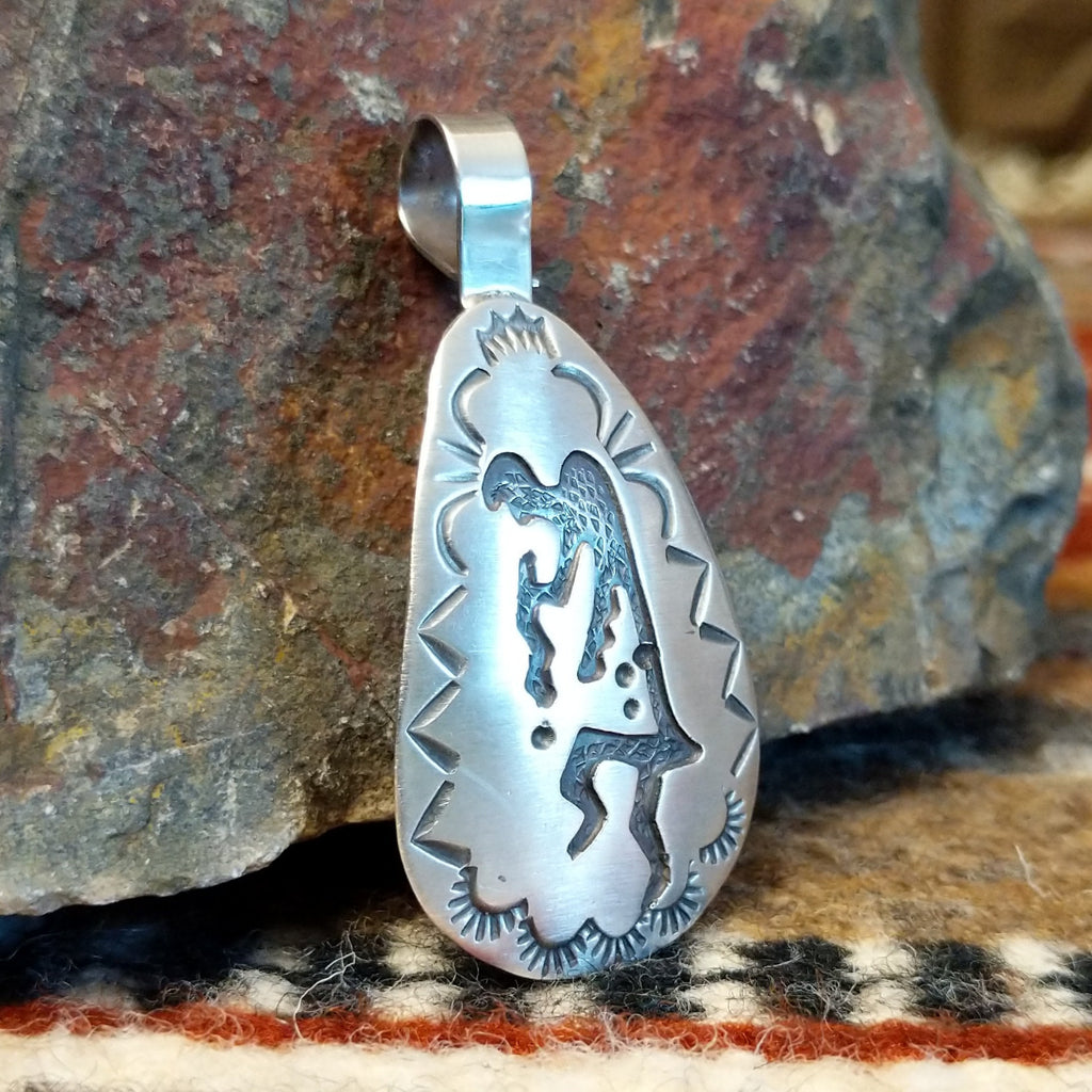 Triangular sterling silver pendant with kokopelli figure and geometric designs on the surface.