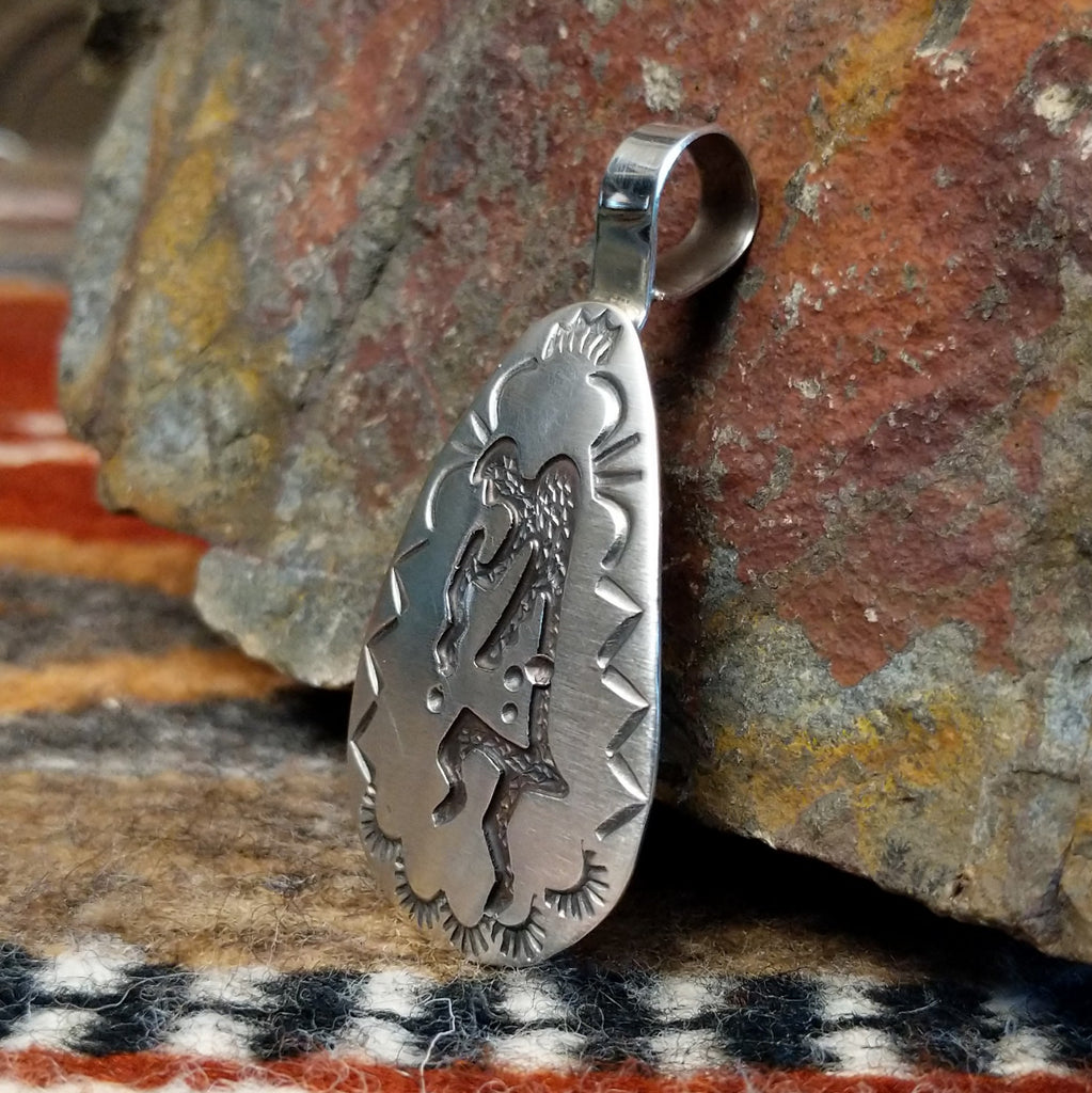 Triangular sterling silver pendant with kokopelli figure and geometric designs on the surface.