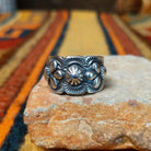 This elegant Silver Ring by Raymond Coriz features a wide silver band with a raised central sunburst, symmetrical silver accents, detailed stamping, and oxidized detailing.