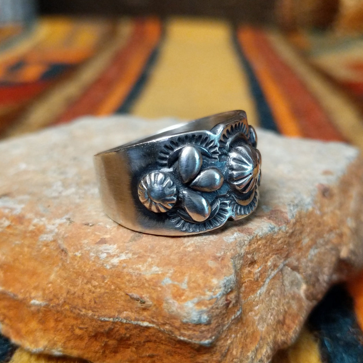 This elegant Silver Ring by Raymond Coriz features a wide silver band with a raised central sunburst, symmetrical silver accents, detailed stamping, and oxidized detailing; side view.