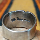 This elegant Silver Ring by Raymond Coriz features a wide silver band with a raised central sunburst, symmetrical silver accents, detailed stamping, and oxidized detailing; artisan and Sterling Silver stamp.