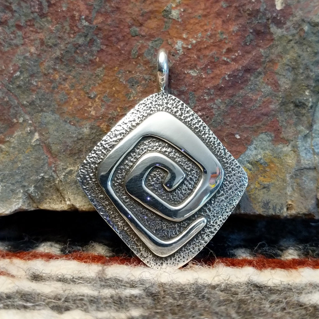 Diamond shaped sterling silver pendant with hammered finish and polished spiral design.