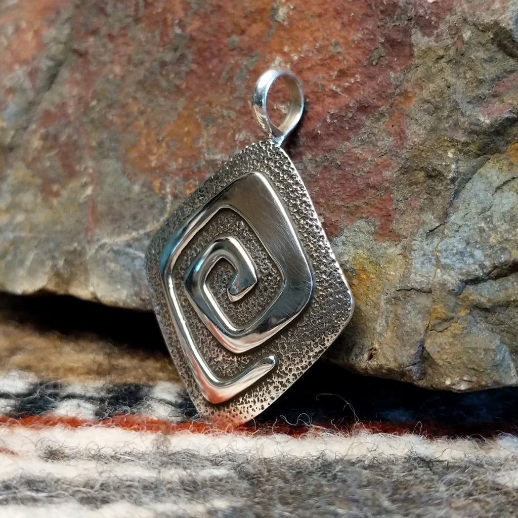 Diamond shaped sterling silver pendant with hammered finish and polished spiral design.