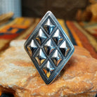 Silver ring by Dakota T. Willie featuring an elongated diamond-shaped face with nine raised, polished studs arranged within textured geometric borders. Straight-on view.