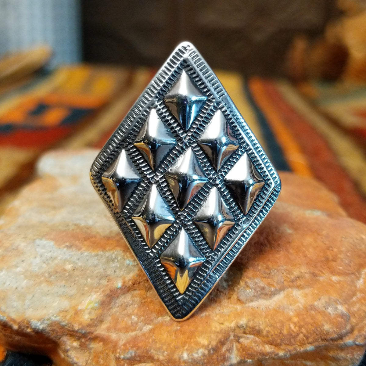 Silver ring by Dakota T. Willie featuring an elongated diamond-shaped face with nine raised, polished studs arranged within textured geometric borders. Straight-on view.