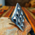 Silver ring by Dakota T. Willie featuring an elongated diamond-shaped face with nine raised, polished studs arranged within textured geometric borders. Ring shown from a 3/4 view.