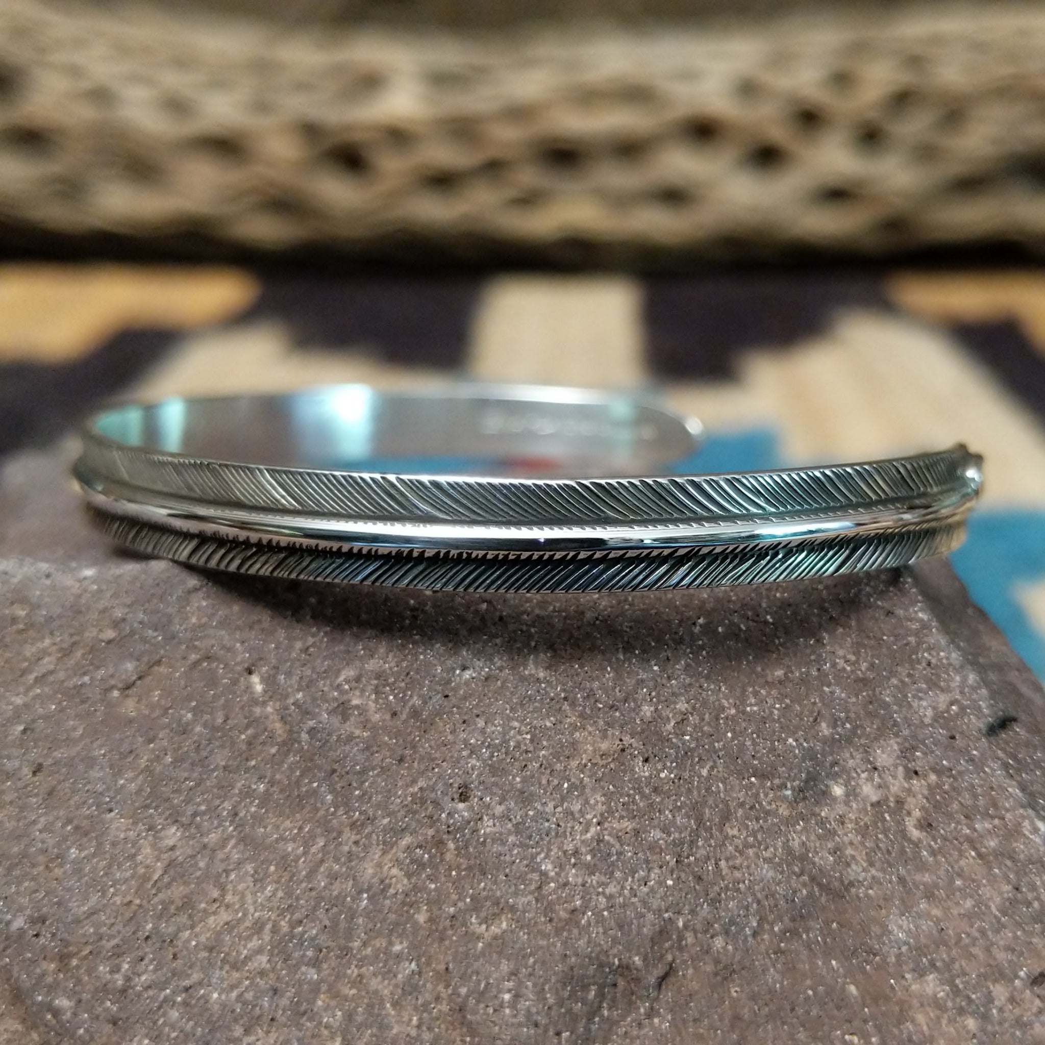 Slender silver feather cuff by Lena Platero, featuring a finely engraved sterling silver feather design in a handcrafted slim open cuff with polished finish.