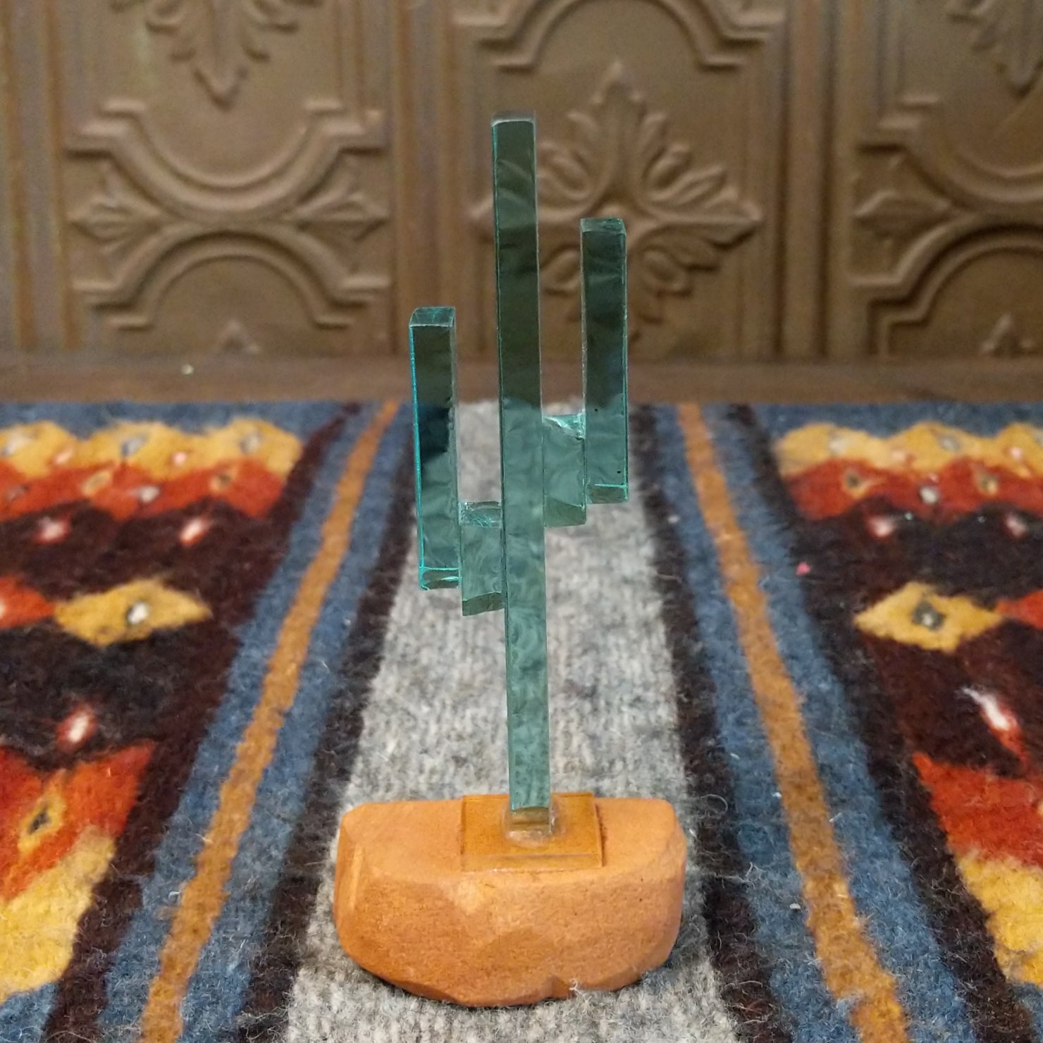 A glass cactus sculpture with translucent aqua glass mounted on a smooth sandstone base.