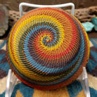 Handwoven small wire art bowl by Bridge for Africa featuring a spiral pattern in recycled wire with mustard yellow, olive green, dusty blue, rust, terracotta, brown, and charcoal tones, ideal for home décor or as a decorative catchall; underside view.