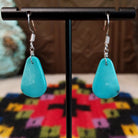 Smooth Navajo turquoise slab earrings featuring polished blue teardrop-shaped stones with minimal natural matrix, suspended from silver hooks.