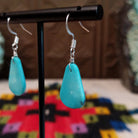 Smooth Navajo turquoise slab earrings featuring polished blue teardrop-shaped stones with minimal natural matrix, suspended from silver hooks; side view.