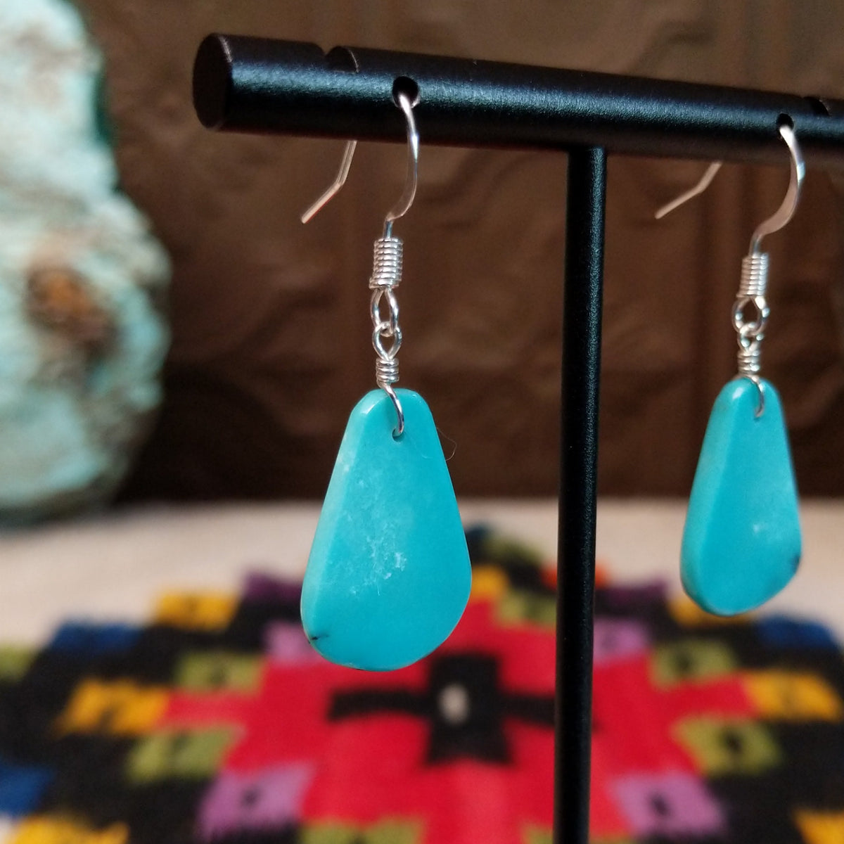 Smooth Navajo turquoise slab earrings featuring polished blue teardrop-shaped stones with minimal natural matrix, suspended from silver hooks; side view.