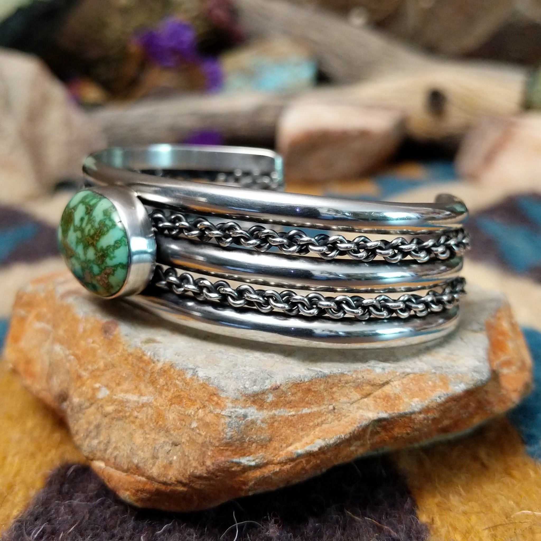 Handcrafted sterling silver cuff by H.R.M. featuring an oval Sonoran Gold turquoise cabochon centered between polished silver bands with dual oxidized chain accents; side view.