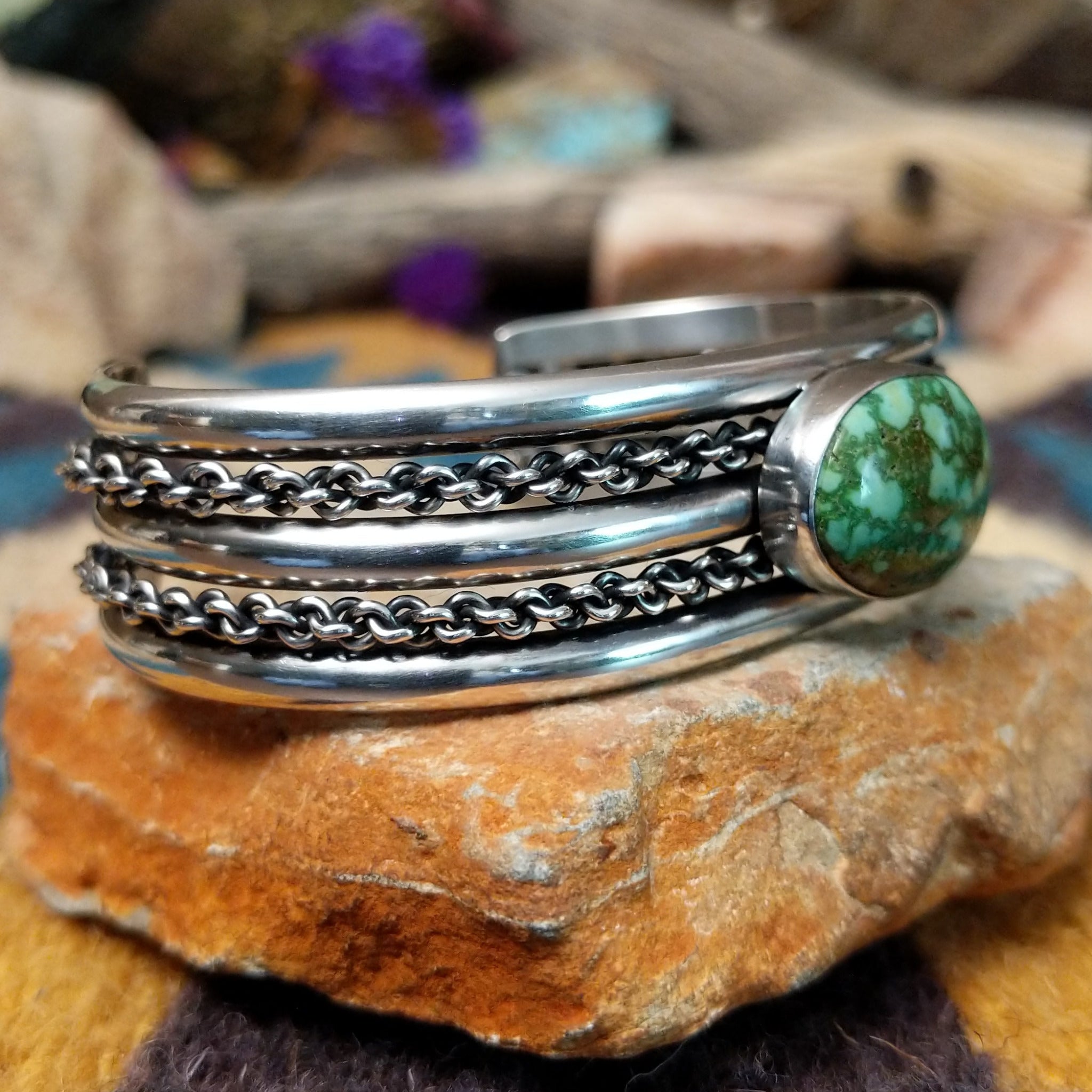 Handcrafted sterling silver cuff by H.R.M. featuring an oval Sonoran Gold turquoise cabochon centered between polished silver bands with dual oxidized chain accents; side view.