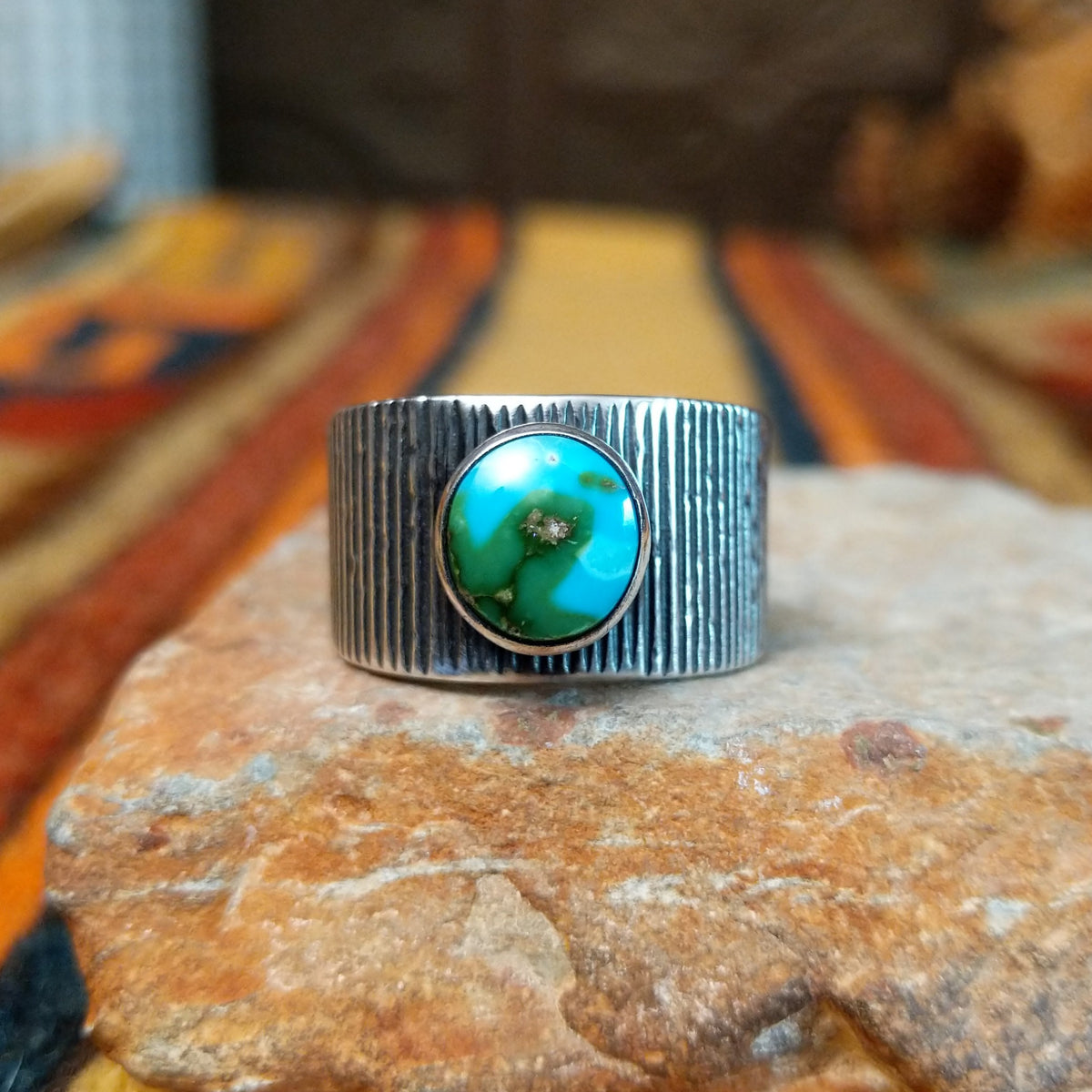 Sonoran Gold Turquoise Ring by Elgin Tom featuring a round blue and green turquoise stone with natural matrix, set in a wide sterling silver band with textured vertical lines.