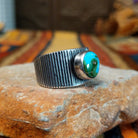 Sonoran Gold Turquoise Ring by Elgin Tom featuring a round blue and green turquoise stone with natural matrix, set in a wide sterling silver band with textured vertical lines; side view.
