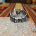 Sonoran Gold Turquoise Ring by Elgin Tom featuring a round blue and green turquoise stone with natural matrix, set in a wide sterling silver band with textured vertical lines; underside view.