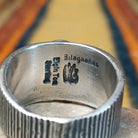 Sonoran Gold Turquoise Ring by Elgin Tom featuring a round blue and green turquoise stone with natural matrix, set in a wide sterling silver band with textured vertical lines; artisan and Sterling Silver stamp.