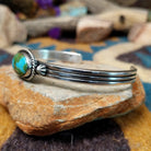 Handcrafted sterling silver cuff by Raymond Coriz featuring an oval Sonoran Gold turquoise cabochon in a twisted rope bezel on a three-wire cuff with hand-stamped fan accents; side view.