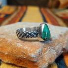Sonoran Gold Turquoise Ring by Raymond Coriz featuring a pear-shaped green turquoise stone with natural matrix, set in sterling silver with a smooth bezel and decorative braided band; side view.