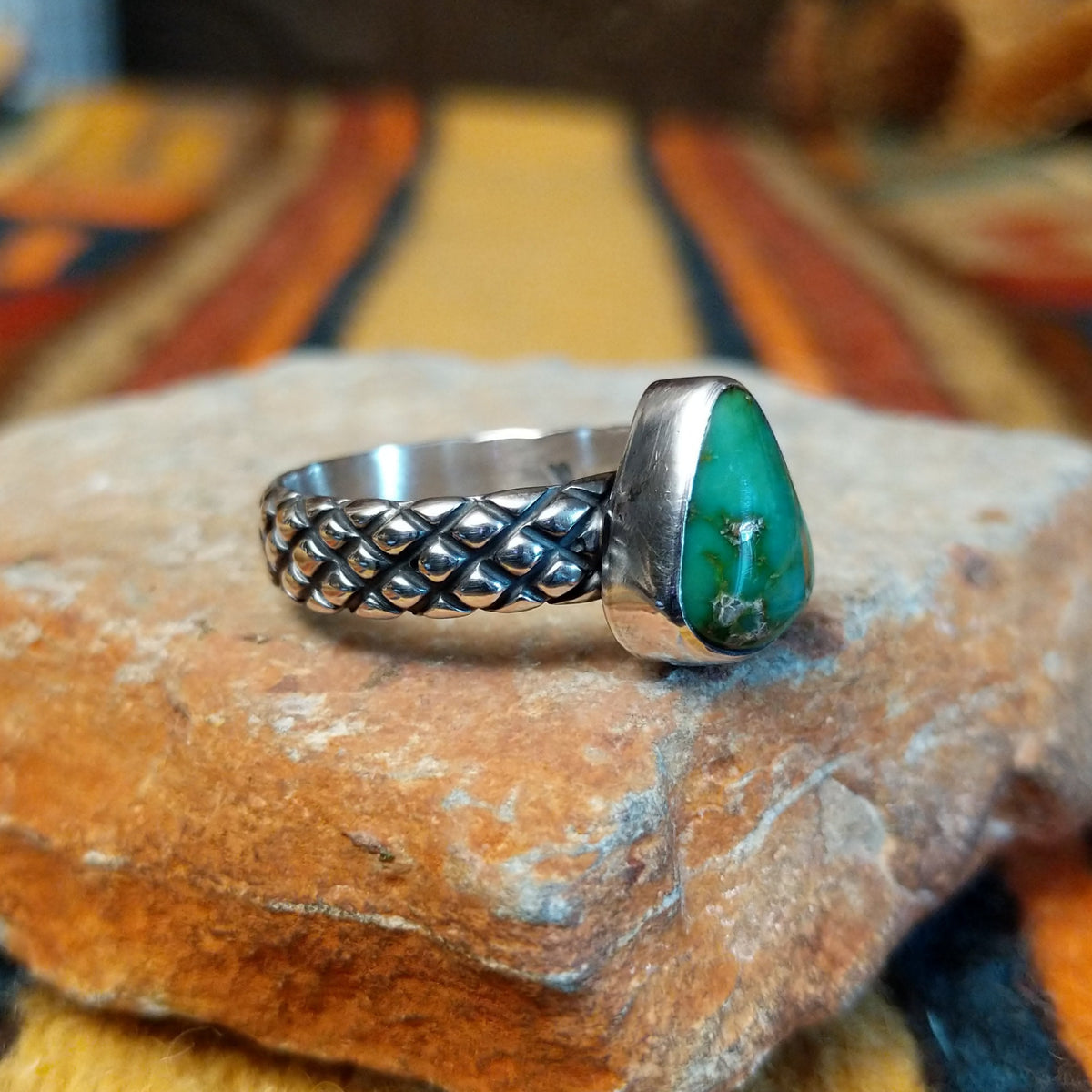 Sonoran Gold Turquoise Ring by Raymond Coriz featuring a pear-shaped green turquoise stone with natural matrix, set in sterling silver with a smooth bezel and decorative braided band; side view.