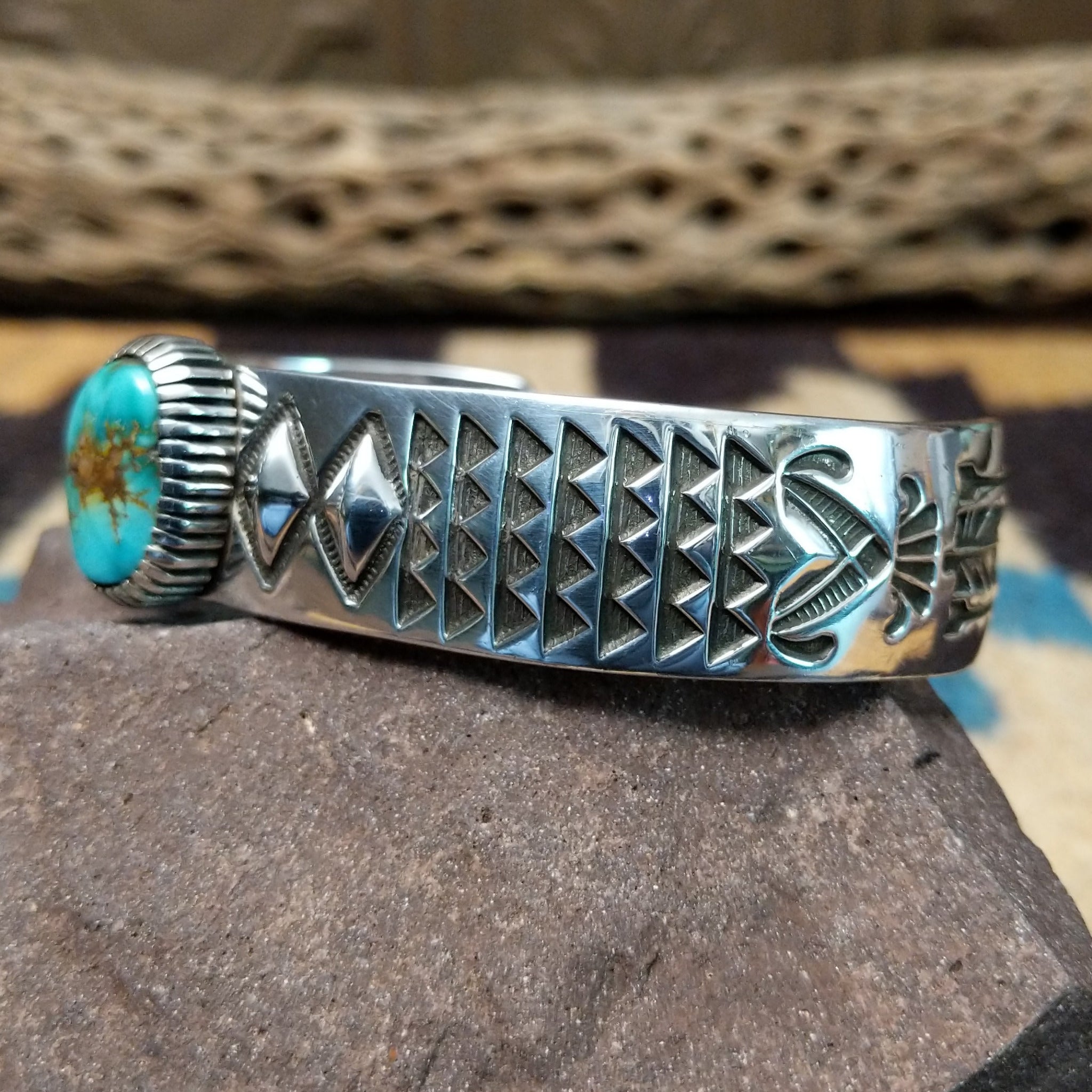 Sonoran Mountain turquoise cuff by Rydel Victor Curtis, featuring an oval blue Sonoran Mountain turquoise stone with natural golden-brown matrix set in a handcrafted sterling silver cuff with intricate geometric stampwork; side view.