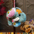 This charming Spearmint Colored Elephant Wool Ornament features a soft green body, pink ears, golden yellow hair, white tusks, blue feet, colorful embroidered details, and a red and white twisted hanging cord.
