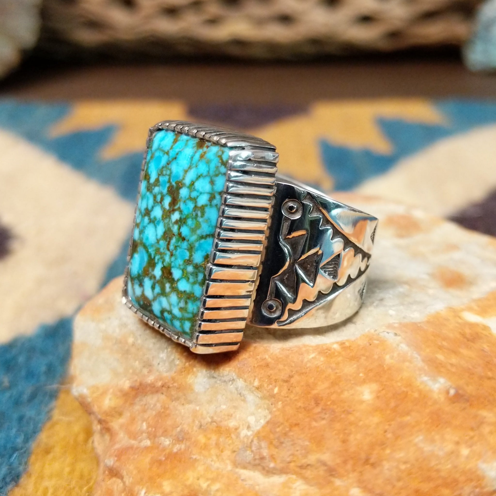 Spiderweb Kingman Turquoise Ring by Joe Piaso Jr. featuring a large rectangular sky-blue Kingman turquoise stone with an intricate dark spiderweb matrix, set in a sterling silver serrated bezel with an openwork silver band, displayed on a natural stone; side view.
