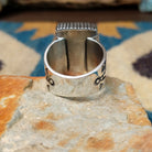 Spiderweb Kingman Turquoise Ring by Joe Piaso Jr. featuring a large rectangular sky-blue Kingman turquoise stone with an intricate dark spiderweb matrix, set in a sterling silver serrated bezel with an openwork silver band, displayed on a natural stone; underside view.