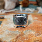 Handcrafted sterling silver ring by Raymond Coriz featuring an intricate rectangular spiral design with stamped details, an oxidized background, and a wide polished silver band.