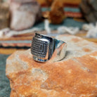 Handcrafted sterling silver ring by Raymond Coriz featuring an intricate rectangular spiral design with stamped details, an oxidized background, and a wide polished silver band; side view.