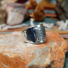 Handcrafted sterling silver ring by Raymond Coriz featuring an intricate rectangular spiral design with stamped details, an oxidized background, and a wide polished silver band; side view.