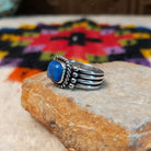 This Square Lapis Ring by Raymond Coriz features a square blue lapis stone set in sterling silver with a twisted rope border, silver bead accents, and a multi-band design; side view.