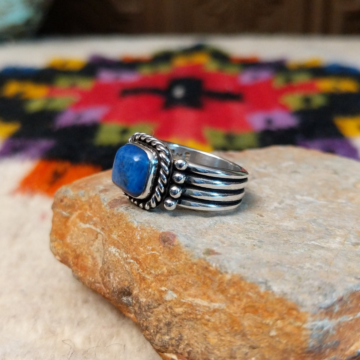 This Square Lapis Ring by Raymond Coriz features a square blue lapis stone set in sterling silver with a twisted rope border, silver bead accents, and a multi-band design; side view.