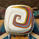 Handwoven square wire art bowl by Bridge for Africa featuring a spiral pattern in recycled wire with ivory, rust, blue, gold, brown, and charcoal tones, ideal for home décor or wall display; underside view.