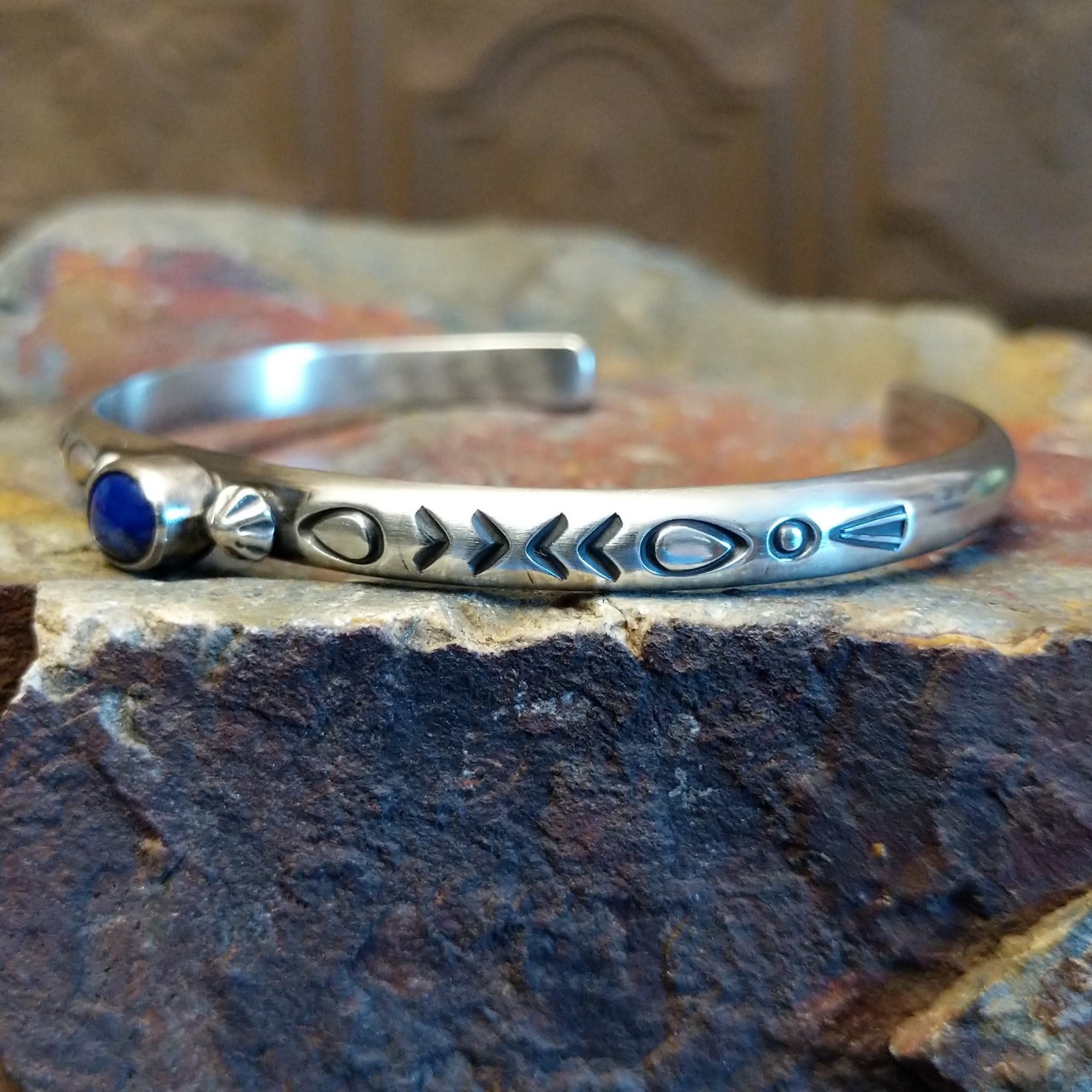 Sterling silver cuff bracelet with intricate stamping along the band and lapis set in the round bezel.